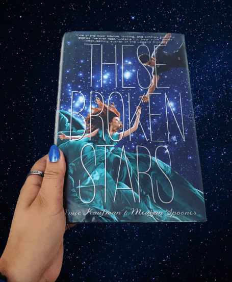 Hand holding book in front of stars
