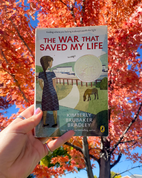 Hand holding book in front of tree