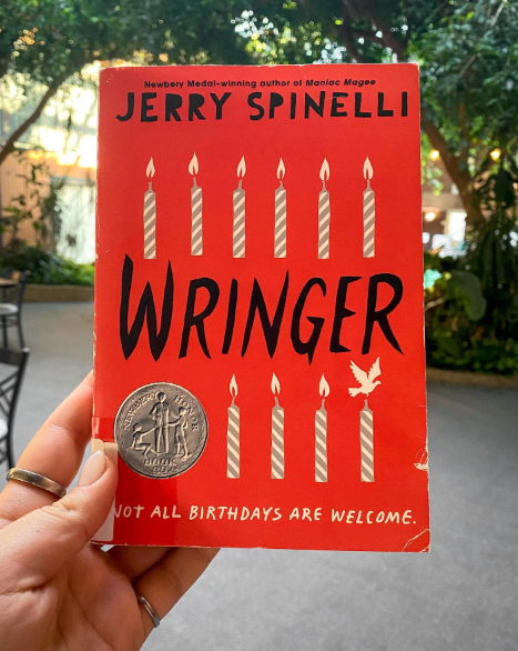 Hand holding book in front of trees