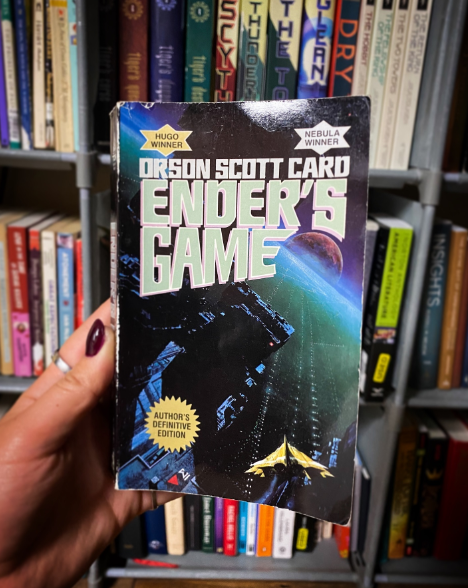 Hand holding book in front of bookshelf