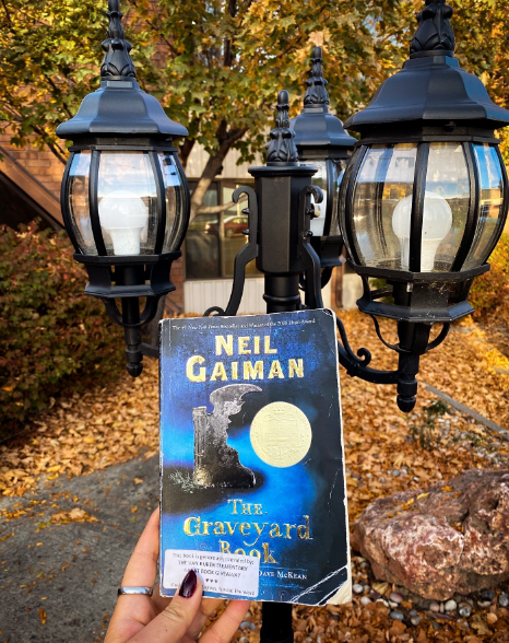 Hand holding book in front of light post and autumn leaves