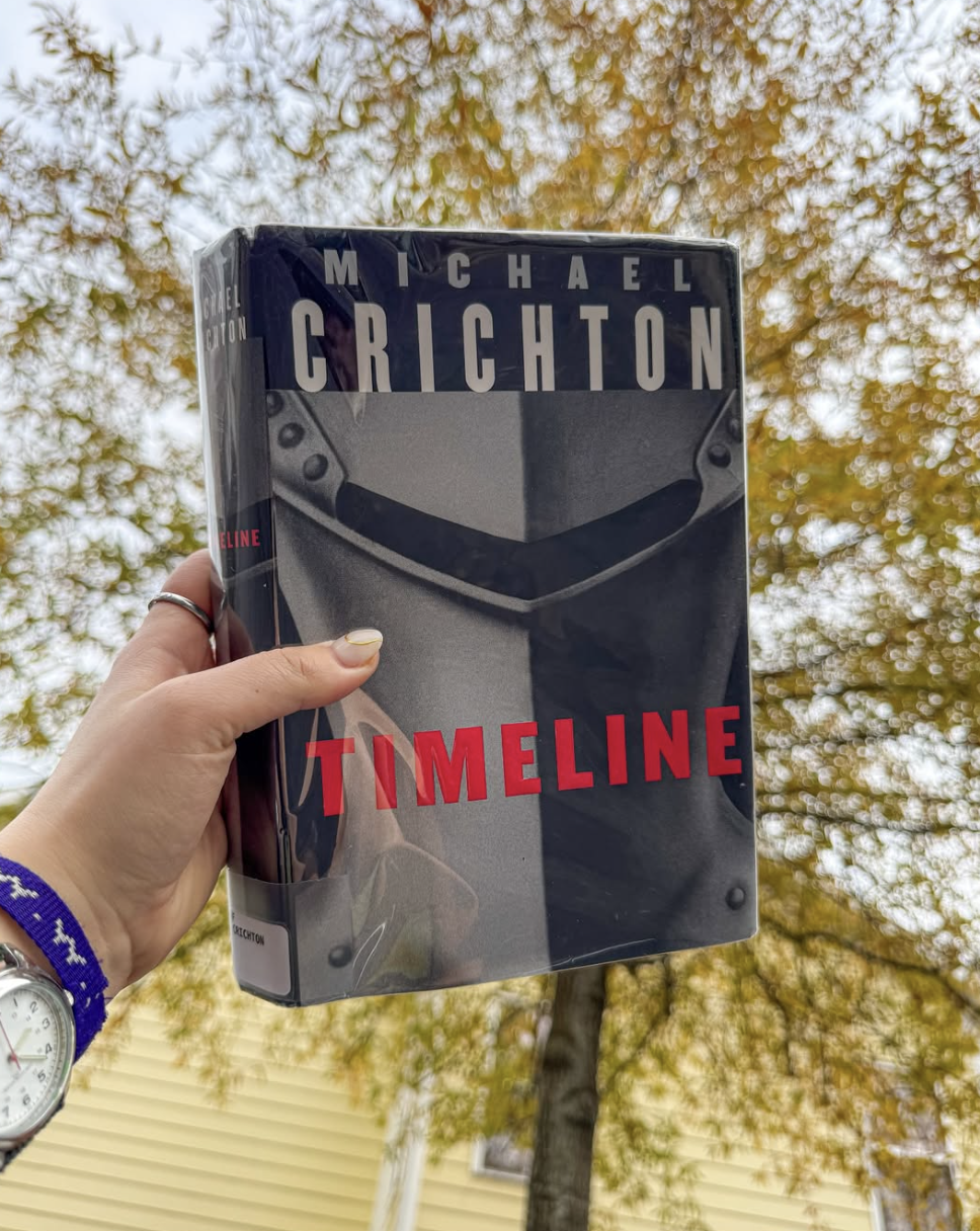 Hand holding book in front of autumn leaves