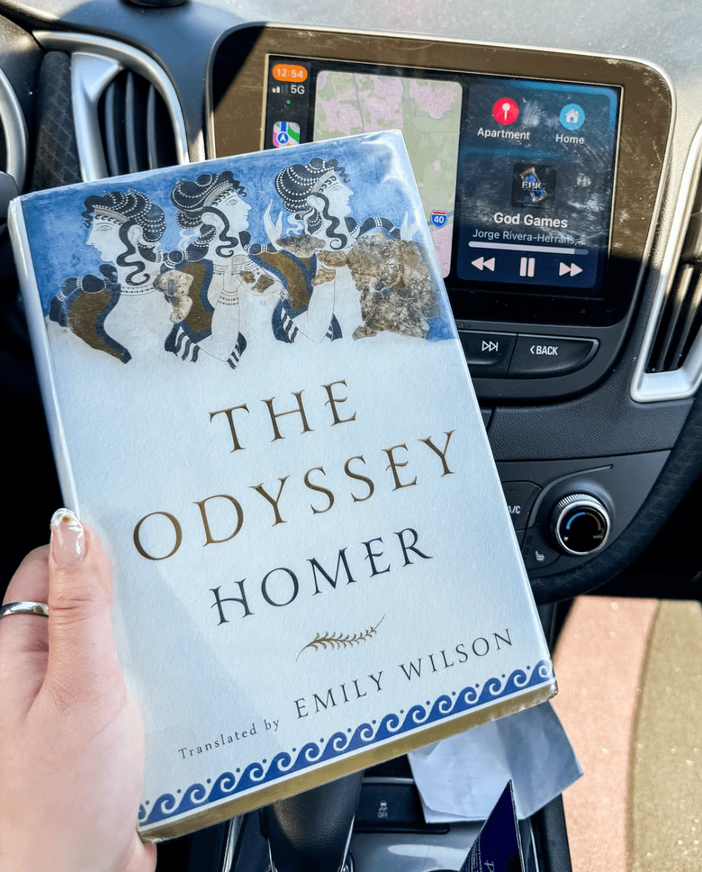 Hand holding a book in front of a car's dashboard