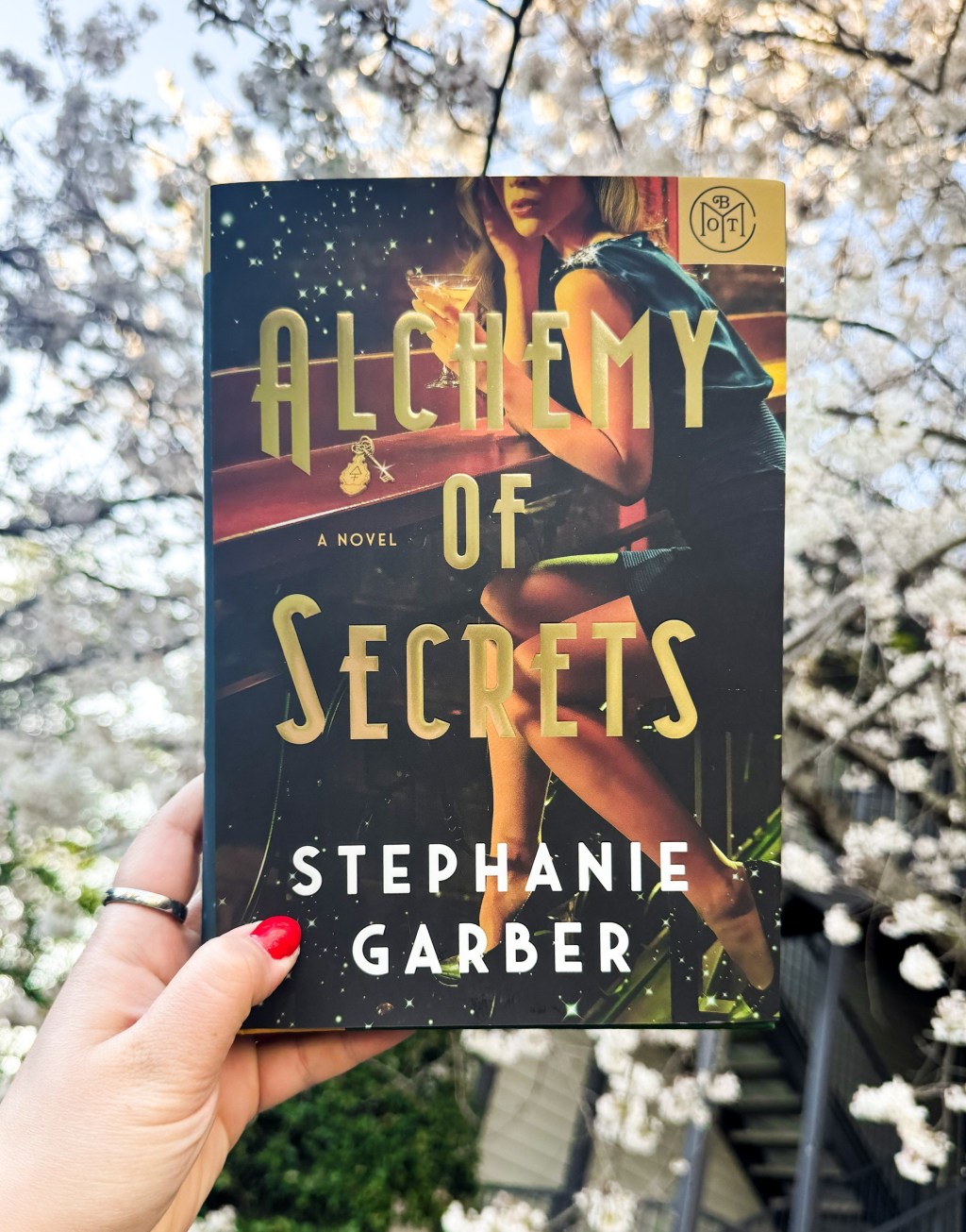 Hand holding book in front of tree with white flowers